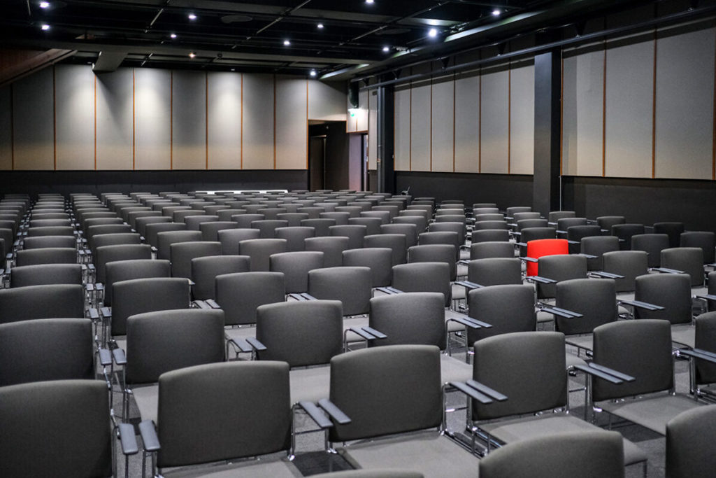 Rebel venue, stor konferansesal, med kinooppsett. Mange grå stoler og en rød stol.